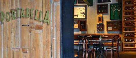 A wooden door with the name "PORTABELLA" and a bistro sign. Inside, there are tables and chairs, a display of wine bottles, and framed items on the wall.