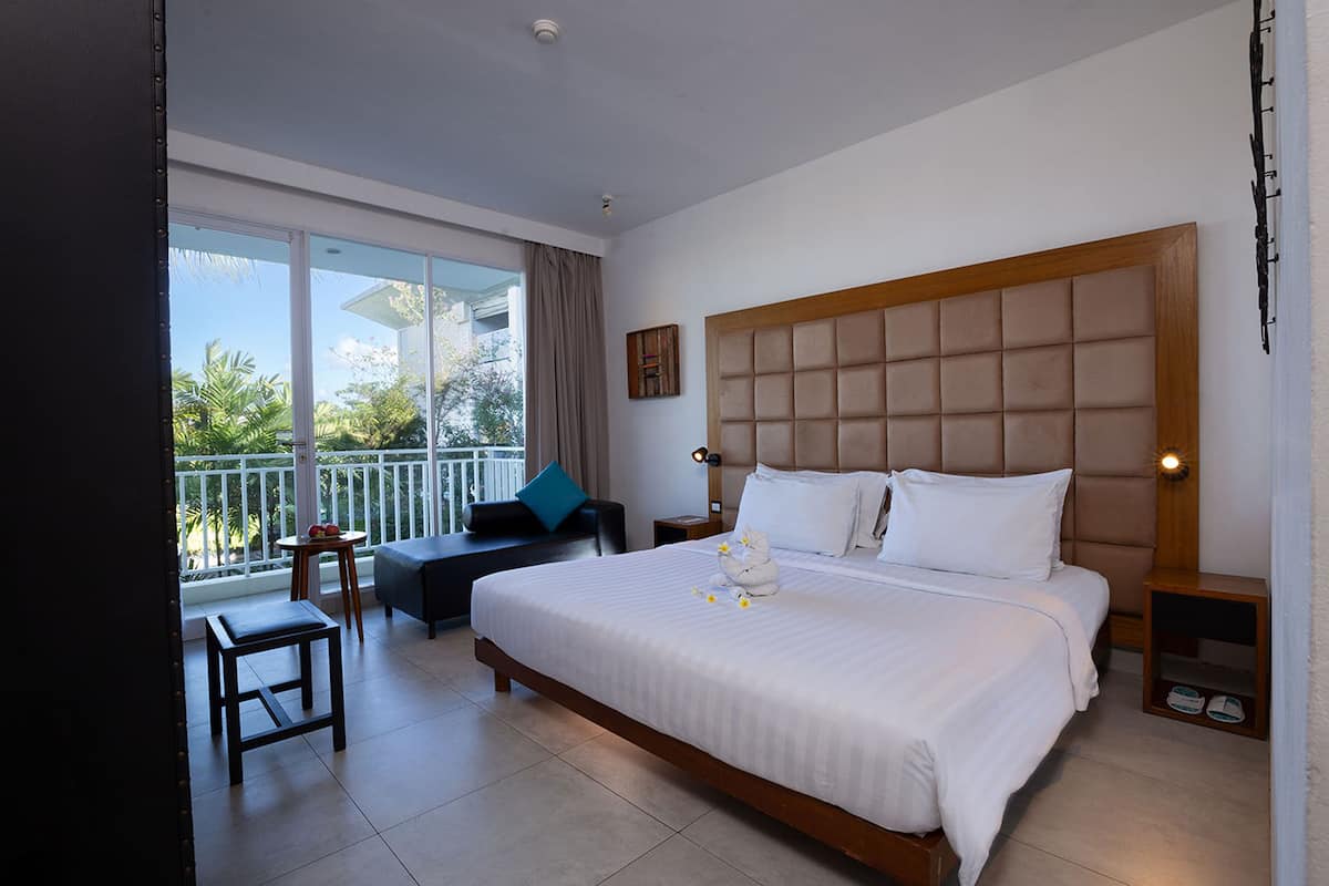 Habitación de hotel con una cama grande, un balcón con vistas, una mesita y una silla.