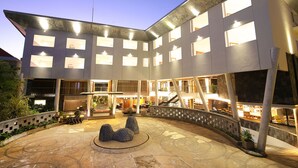 Un edificio moderno con varios pisos, grandes ventanales y un patio central con asientos y plantas.