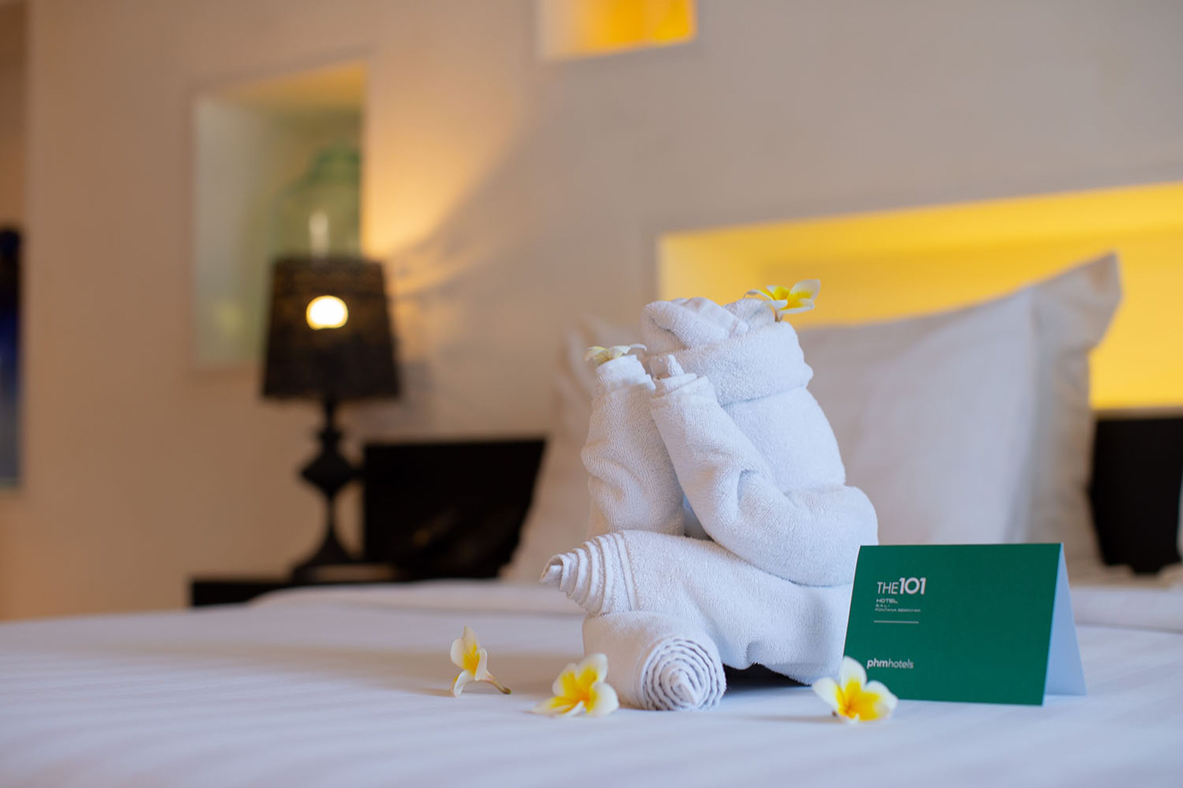 A neatly made bed with a folded towel and a green card on it.