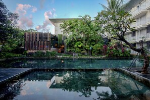 A modern hotel with a glass-bottomed pool surrounded by lush greenery and a multi-story building with balconies. - THE 1O1 Bali Fontana Seminyak (Legian)