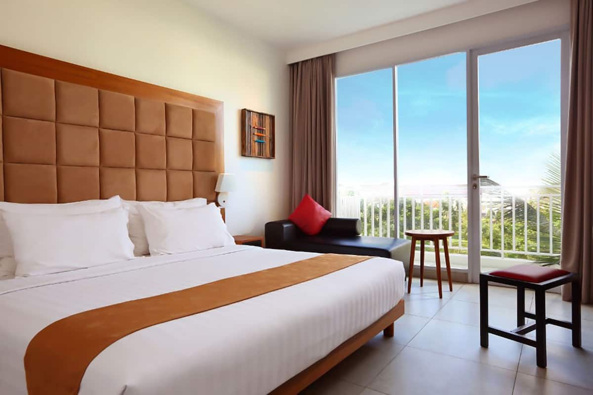 Habitación de hotel con una cama grande, cabecero, balcón con vistas, una mesita pequeña y una silla.