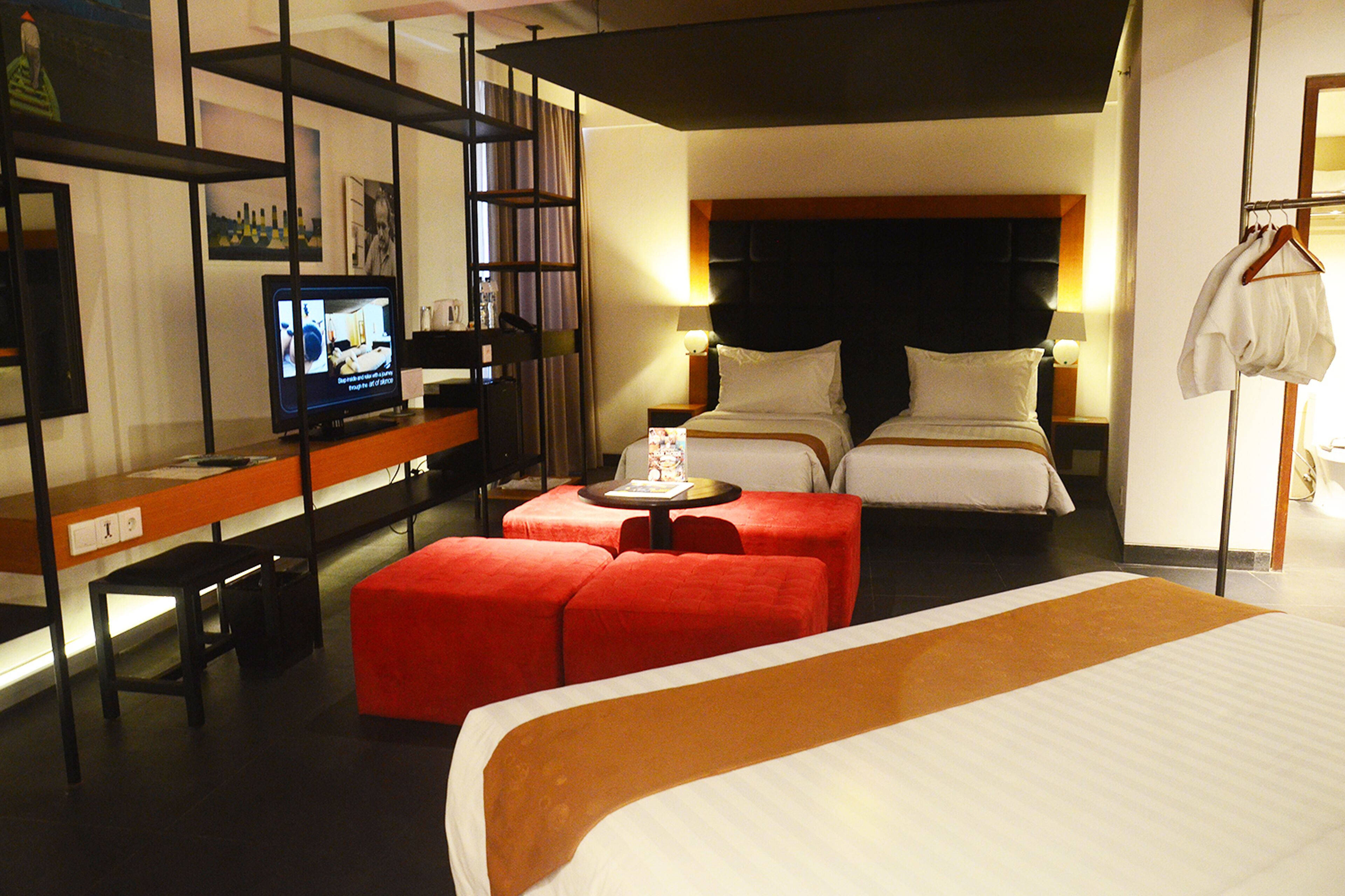 A hotel room with a large bed, a desk with a computer, a red ottoman, and a television on the desk.
