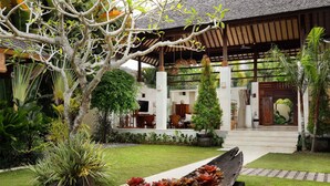 A tropical garden with a wooden deck, a stone pathway, and a variety of plants.