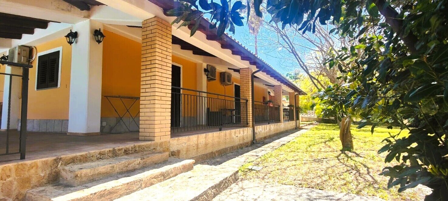 A building with a covered porch, brick columns, and a small garden area.