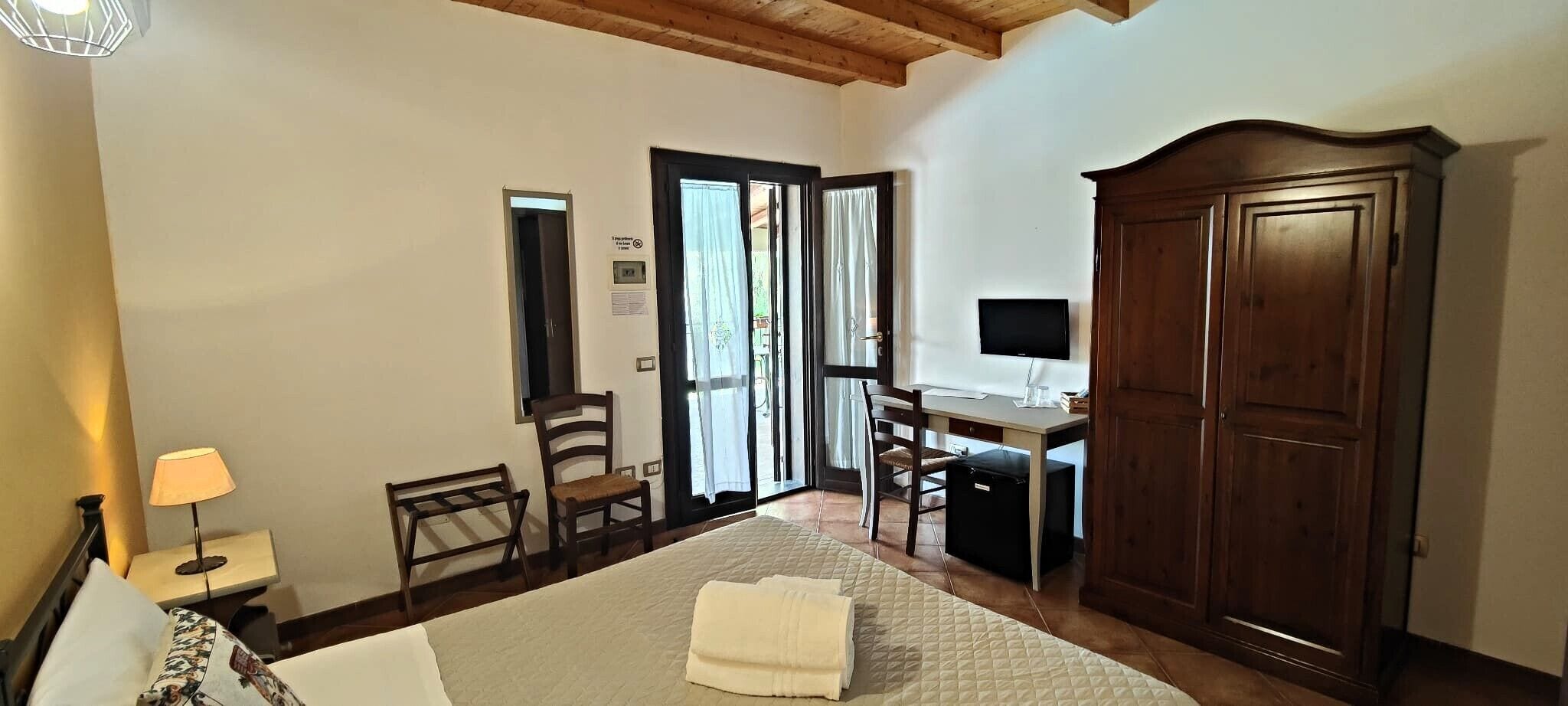 A hotel room with a bed, desk, chair, wardrobe, and a television.