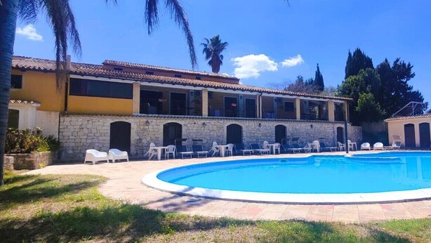 Una piscina con sillas de descanso, un muro de piedra y un edificio con ventanas y balcones.