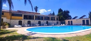 A swimming pool with lounge chairs, a stone wall, and a building with multiple windows and balconies. - Azienda Agrituristica Le Chiuse (Augusta)