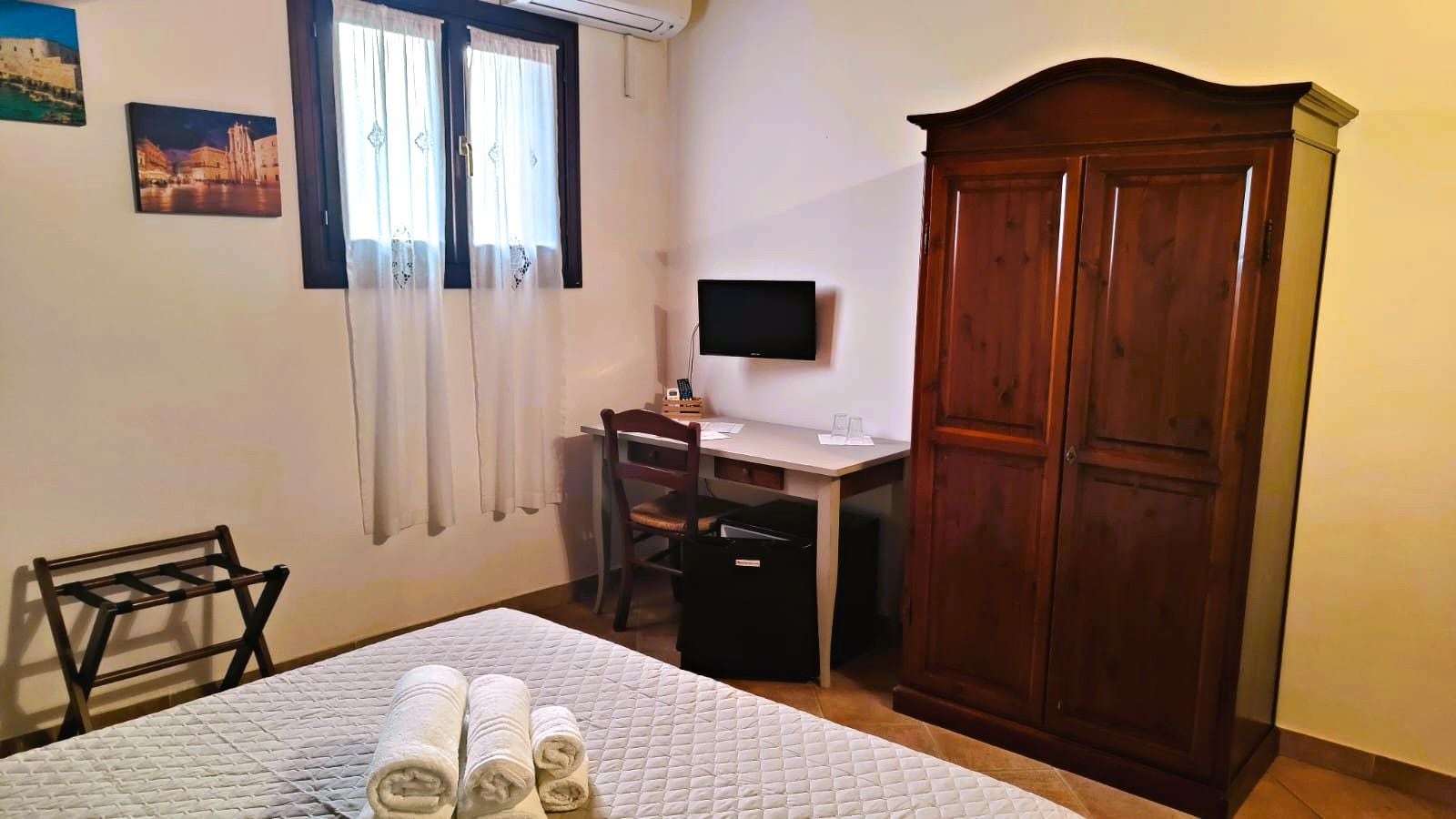 A bedroom with a bed, a desk with a chair, a wardrobe, and a television.