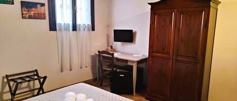 A bedroom with a bed, a desk with a chair, a wardrobe, and a television.
