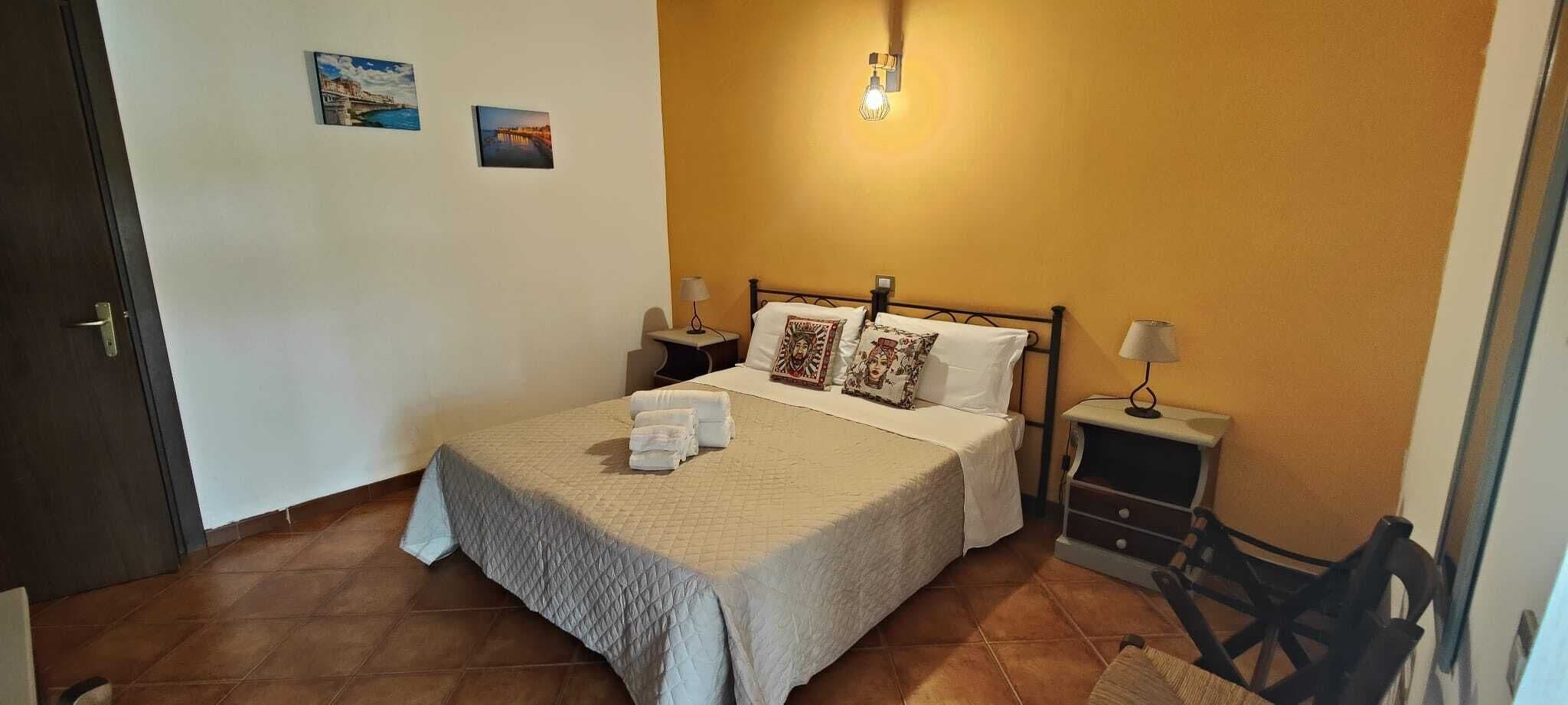A neatly made bed with white linens, two bedside tables with lamps, and a wall-mounted light fixture.