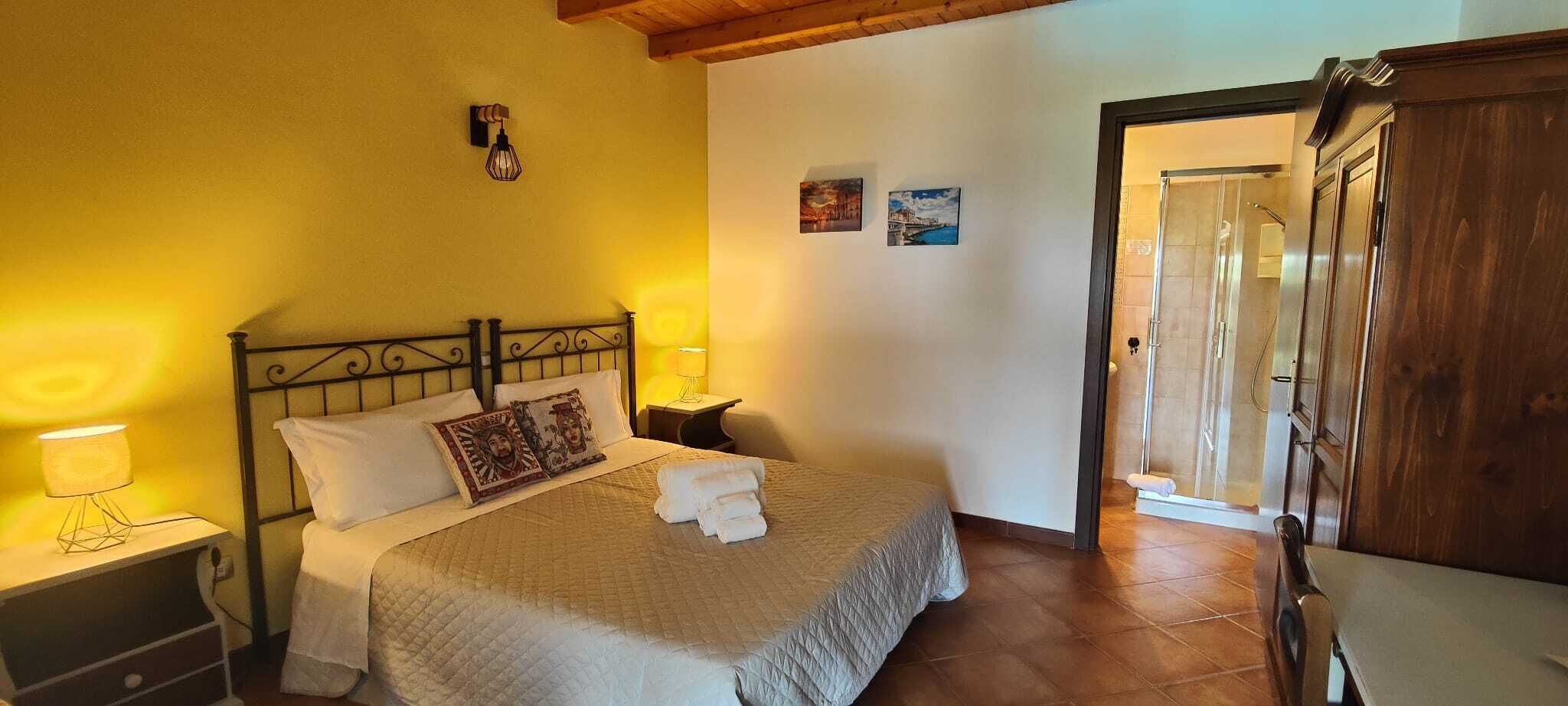 Un dormitorio con cama, lámparas de noche, un armario de madera y una puerta que da a otra habitación.