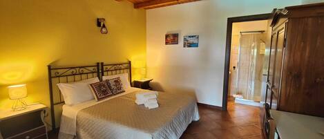 Un dormitorio con cama, lámparas de noche, un armario de madera y una puerta que da a otra habitación.