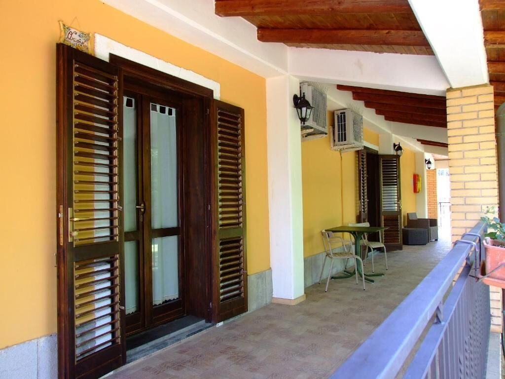 A covered outdoor area with a table and chairs, a wooden door with shutters, and air conditioning units.
