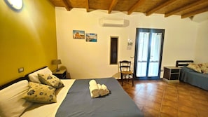 Ein Hotelzimmer mit Bett, Stuhl, Schreibtisch, einem kleinen Tisch und einer Tür zu einem Außenbereich.