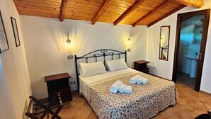 Un dormitorio con cama, mesitas de noche, techo de madera y baño visible a través de una puerta abierta.