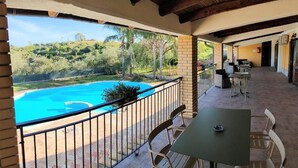 Un espacio al aire libre cubierto con piscina, una mesa con sillas y vistas a un paisaje montañoso.