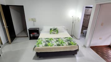 Un dormitorio con cama, mesita de noche y tocador. Hay una puerta que da a otra habitación y una ventana con vistas.
