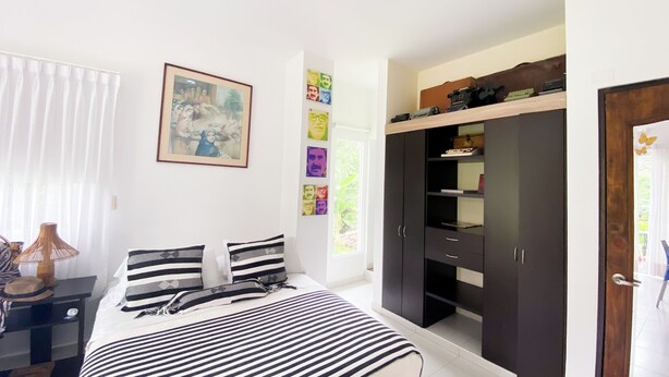 Ein Schlafzimmer mit Bett, Kleiderschrank, Schreibtisch und Fenster mit Jalousien.