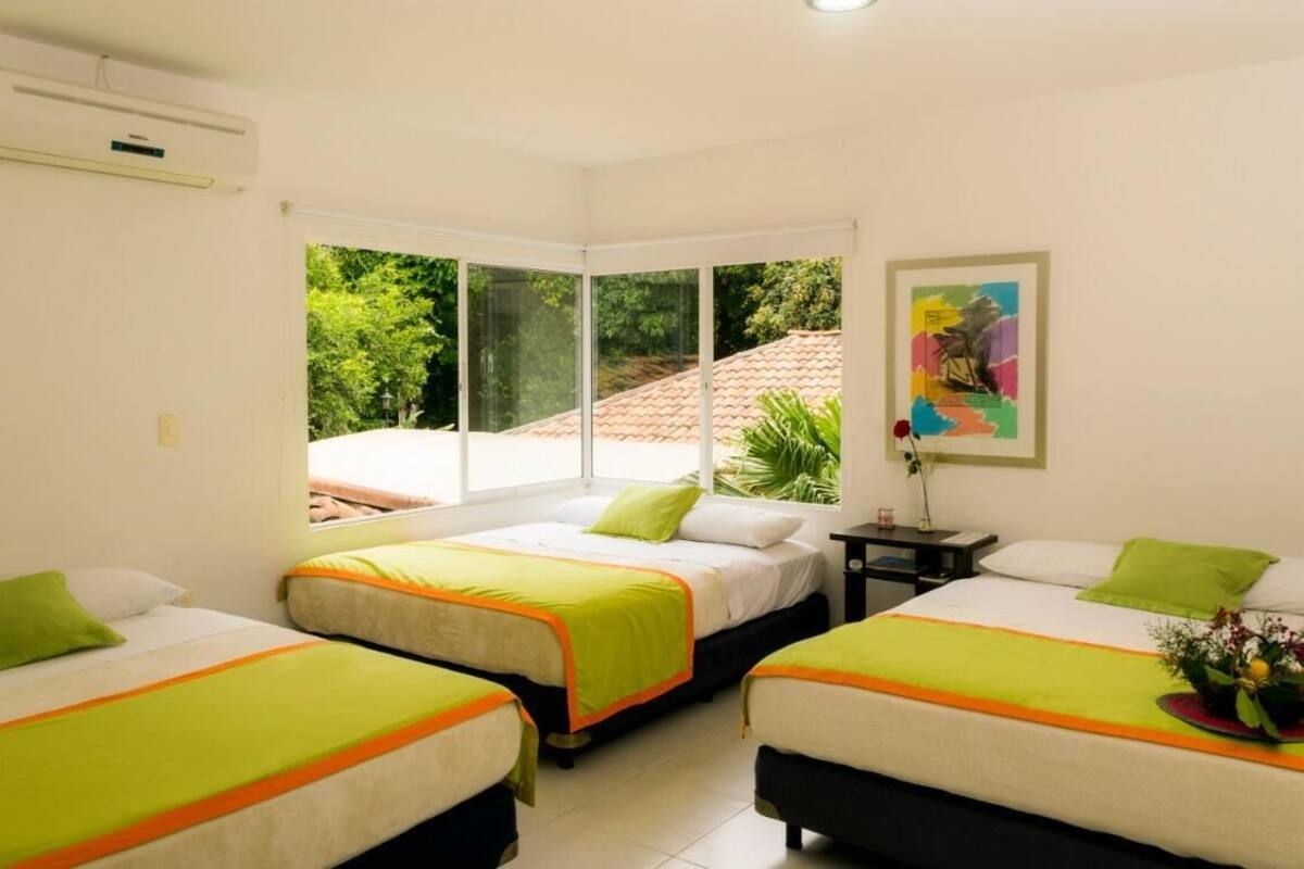 Une chambre d’hôtel avec deux lits, une fenêtre donnant sur un paysage verdoyant, un tableau au mur et un appareil de climatisation.