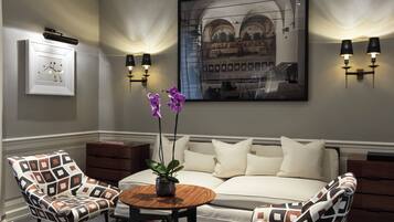A room with a sofa, two patterned armchairs, a small wooden table with a plant, and wall-mounted lighting.