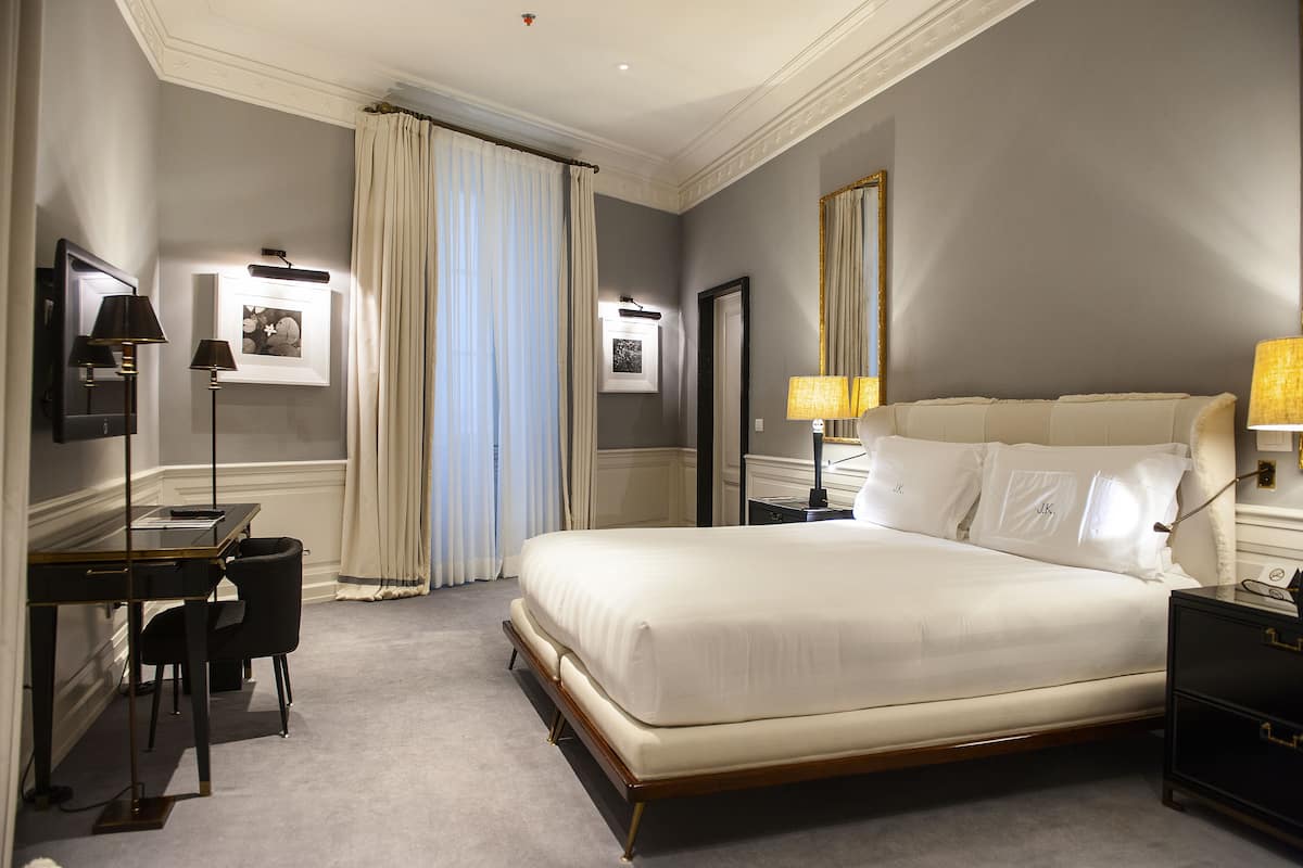 A hotel room with a large bed, a desk, a chair, and a nightstand.