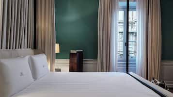 A hotel room with a large bed, a nightstand, a lamp, and a view of a building through the window.