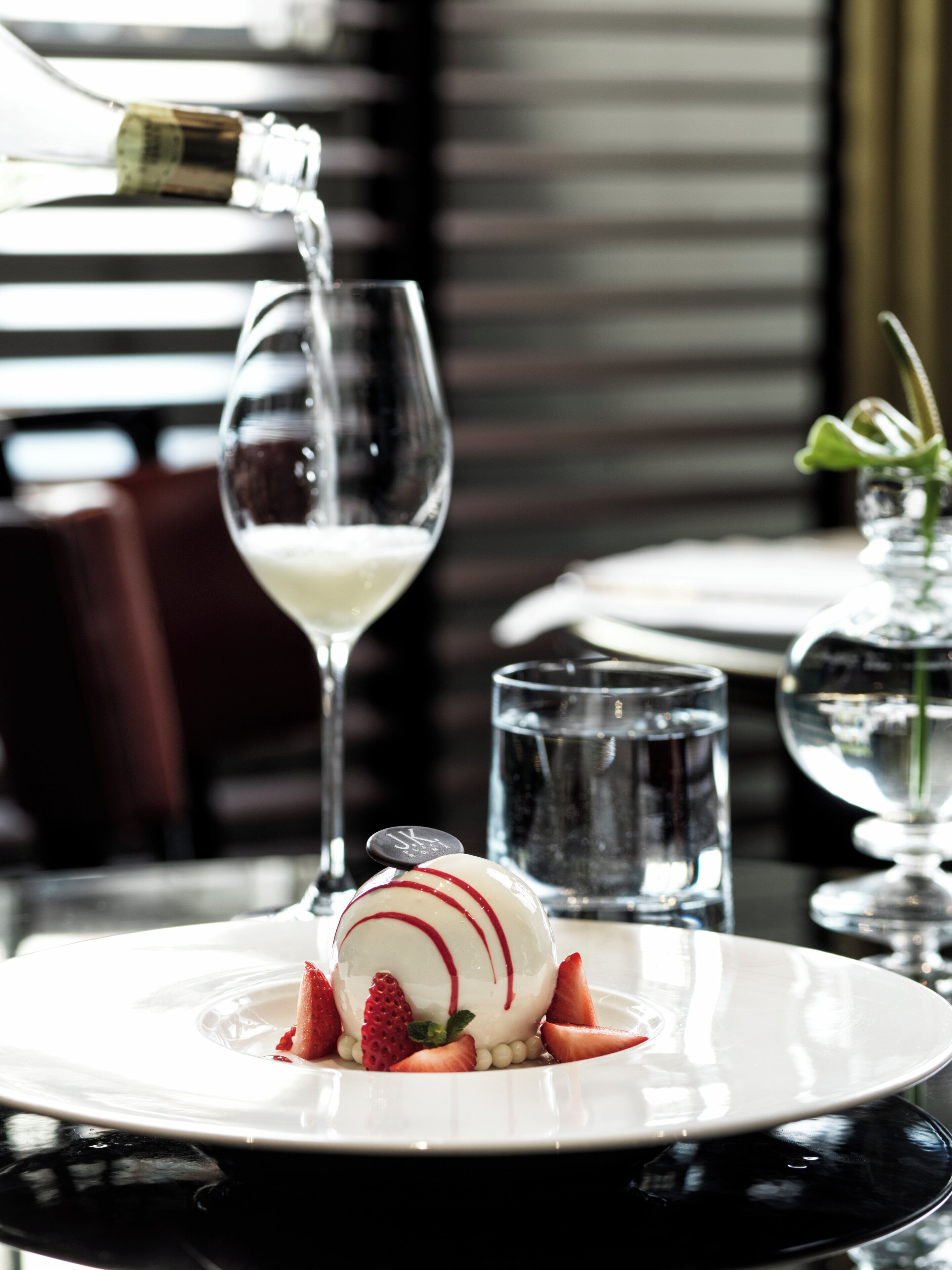 Dessert auf einem Teller mit Erdbeeren und Champagner, der in ein Glas gegossen wird.