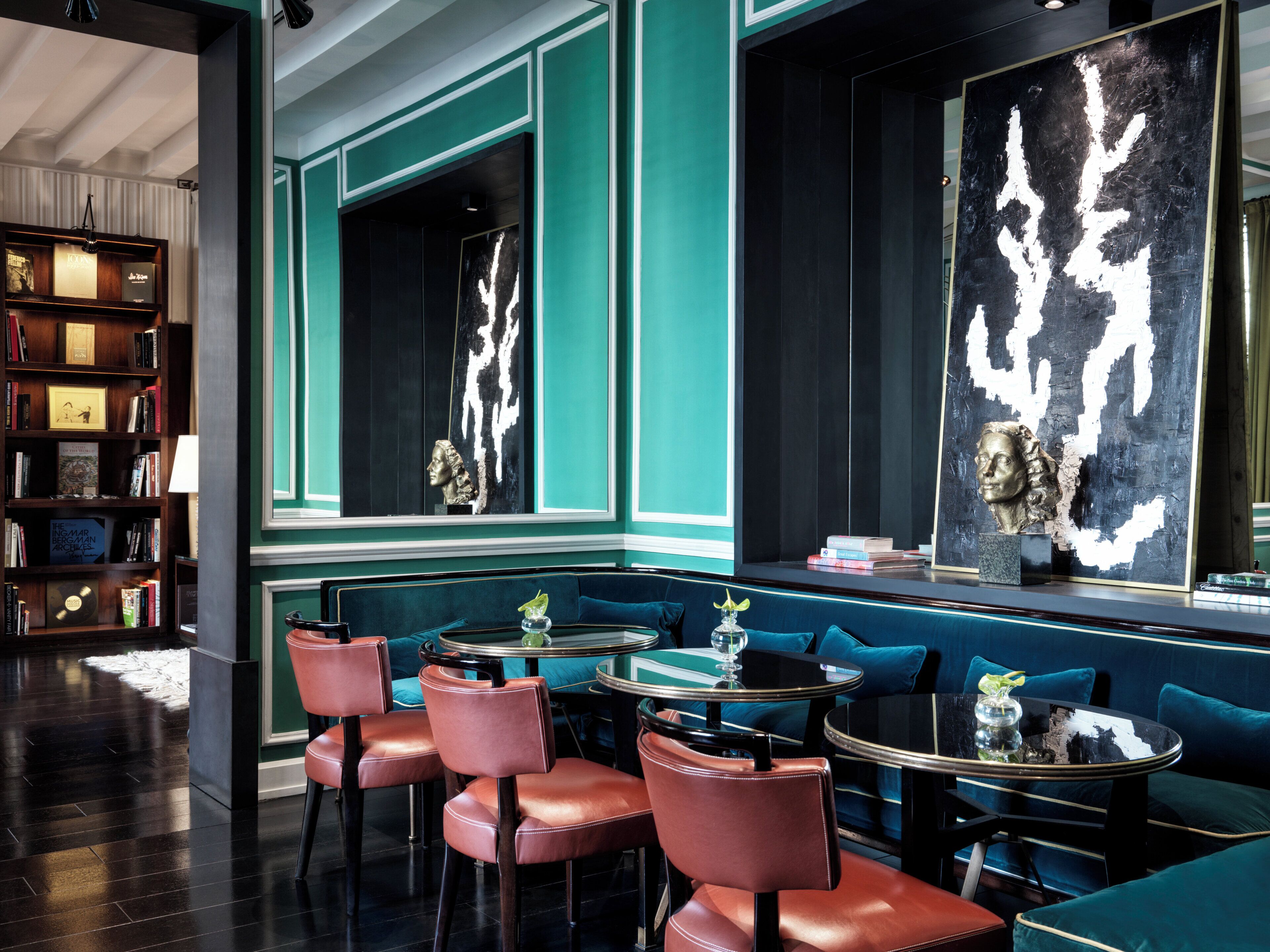 A modern interior with a teal accent wall, a bookshelf, seating area, and artwork.
