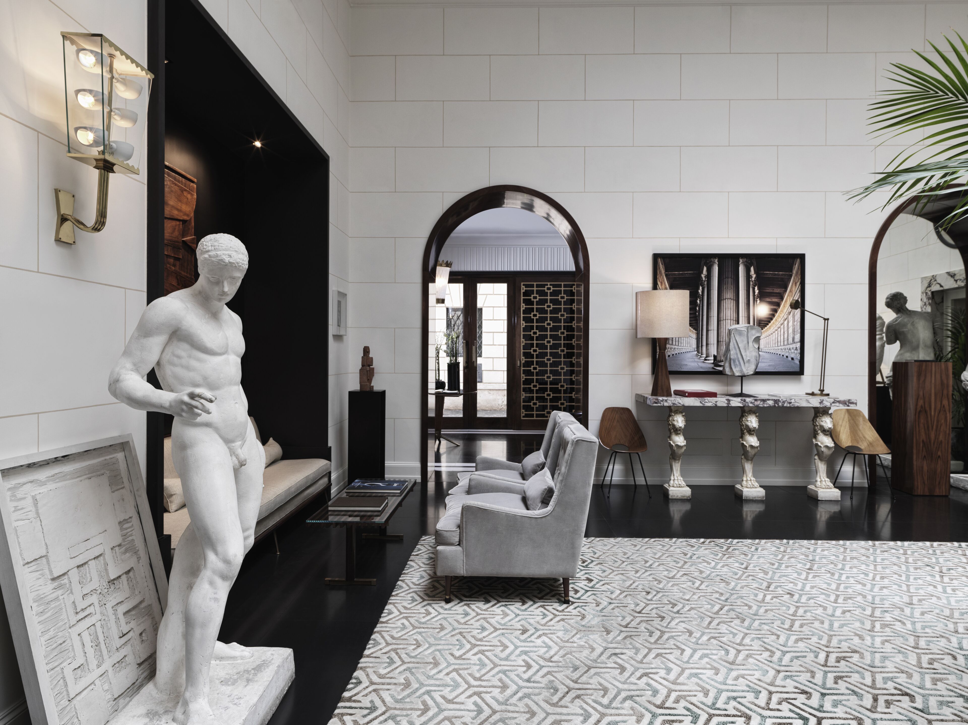A modern lobby with a marble statue, a sofa, a patterned rug, and a large mirror.