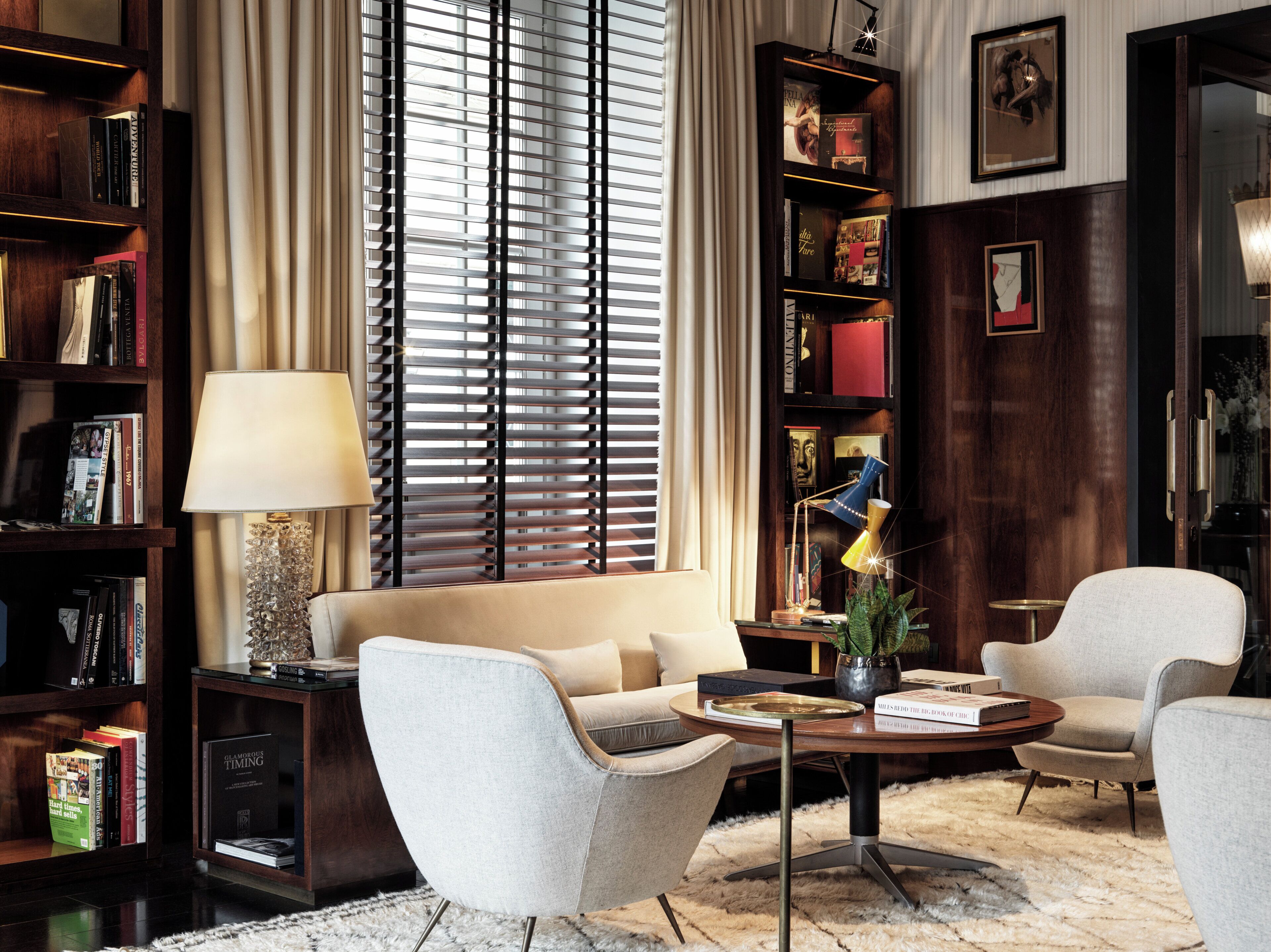 A well-lit living room with a sofa, two armchairs, a coffee table, and a bookshelf filled with books.