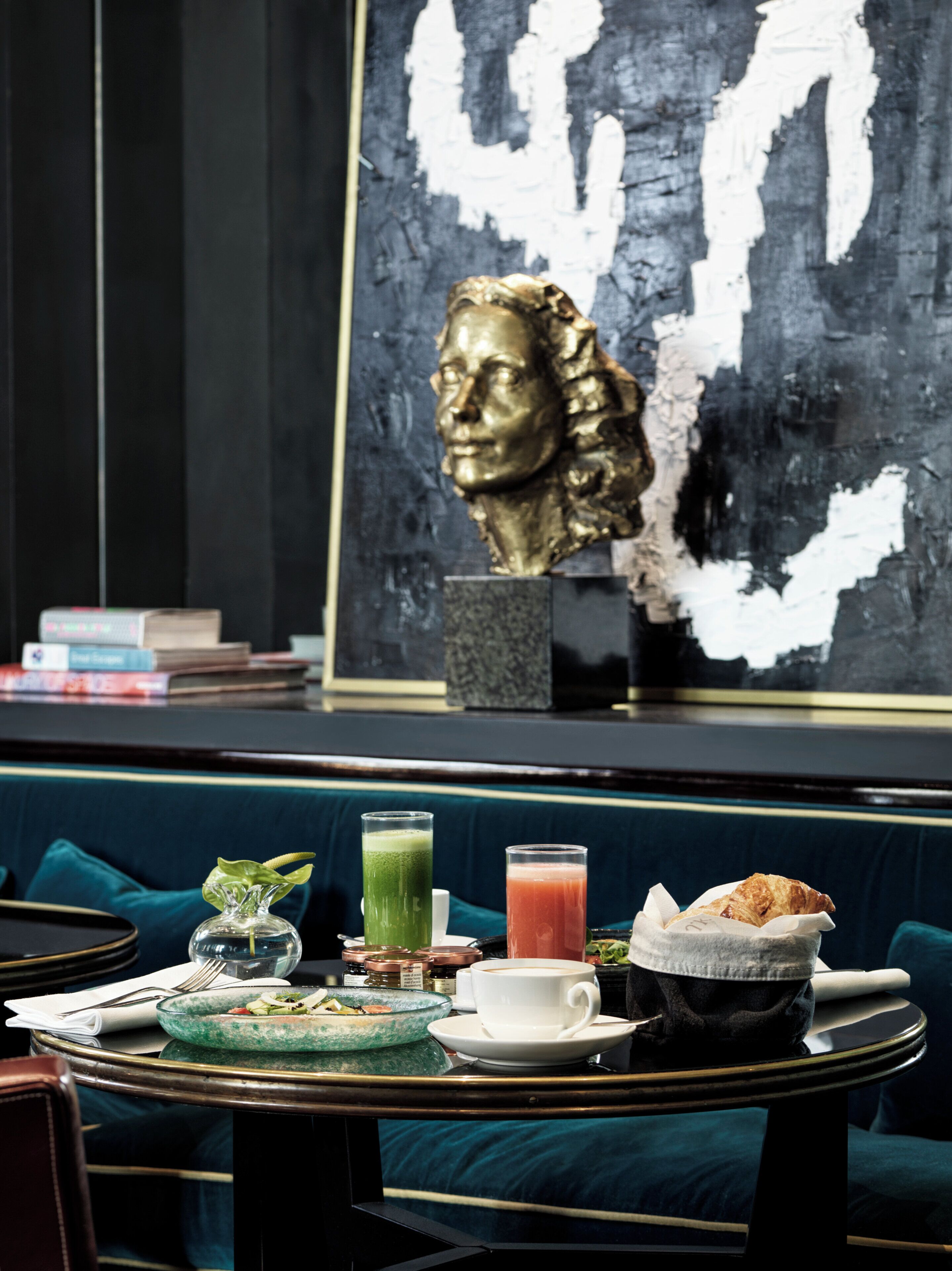 A dining area with a table set for two, a green drink, a red drink, a white cup, and a croissant on a plate.