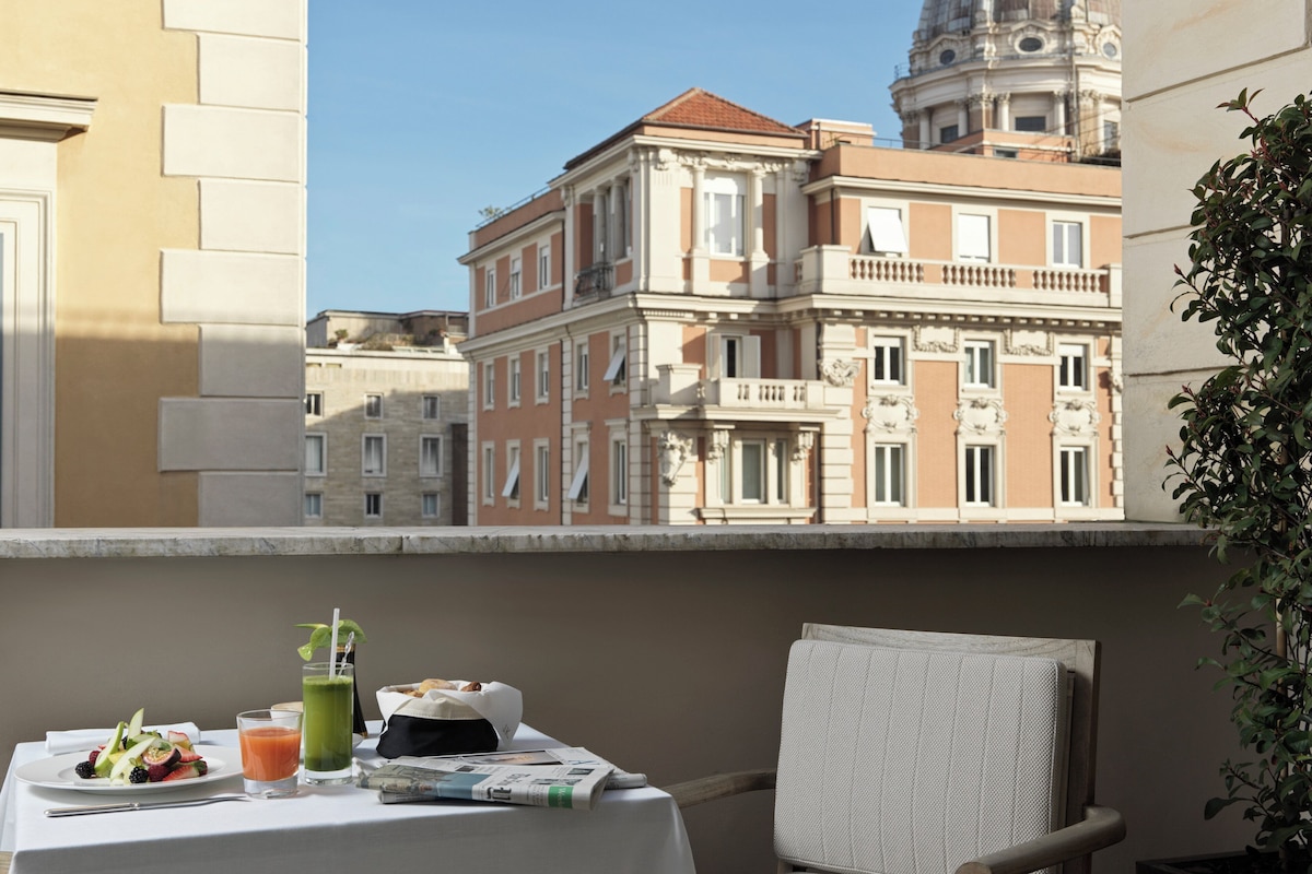 A balcony with a table set for breakfast, a chair, and a view of historic buildings.