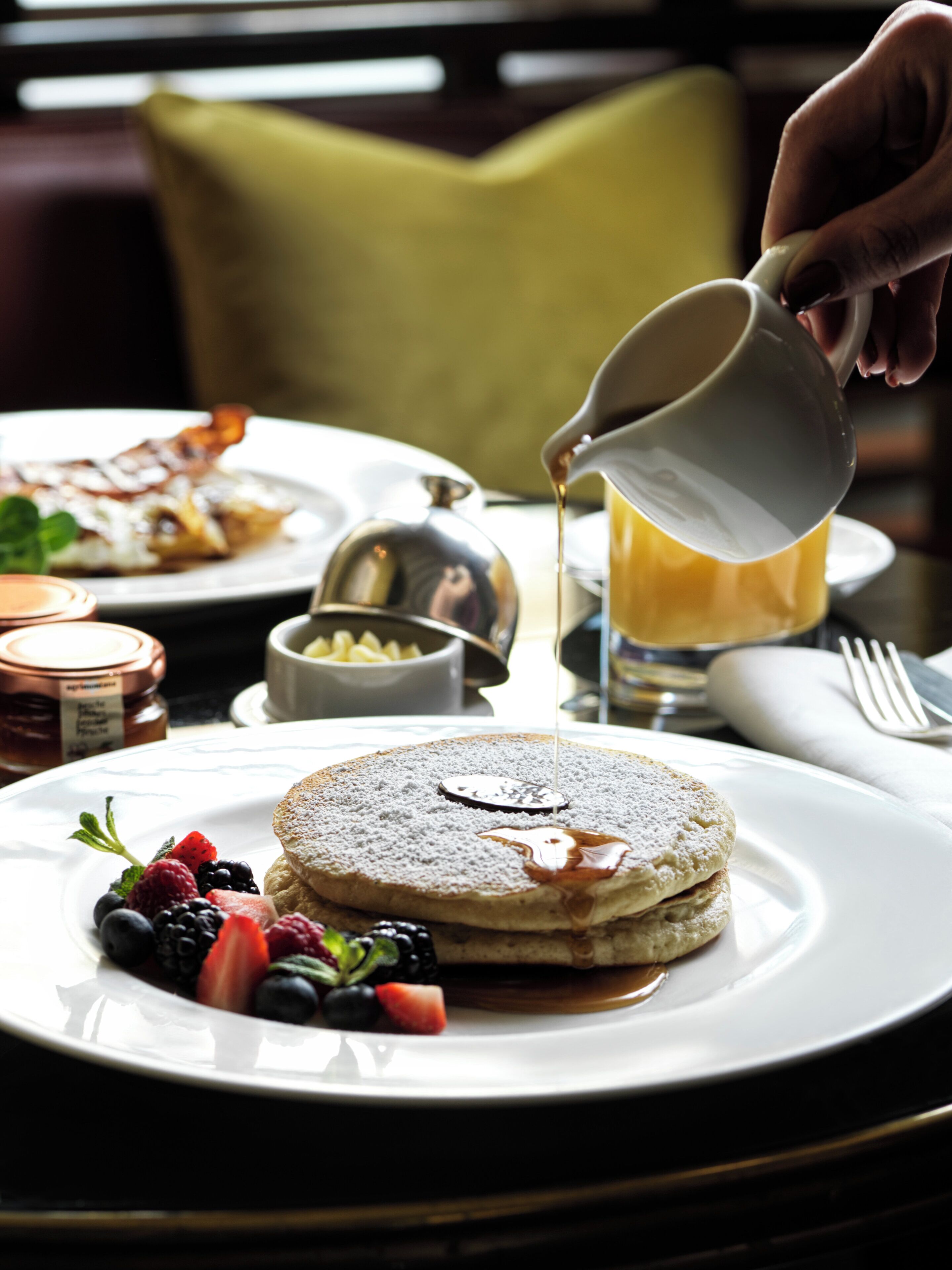 A breakfast setting with pancakes, syrup, and fresh berries on a plate.
