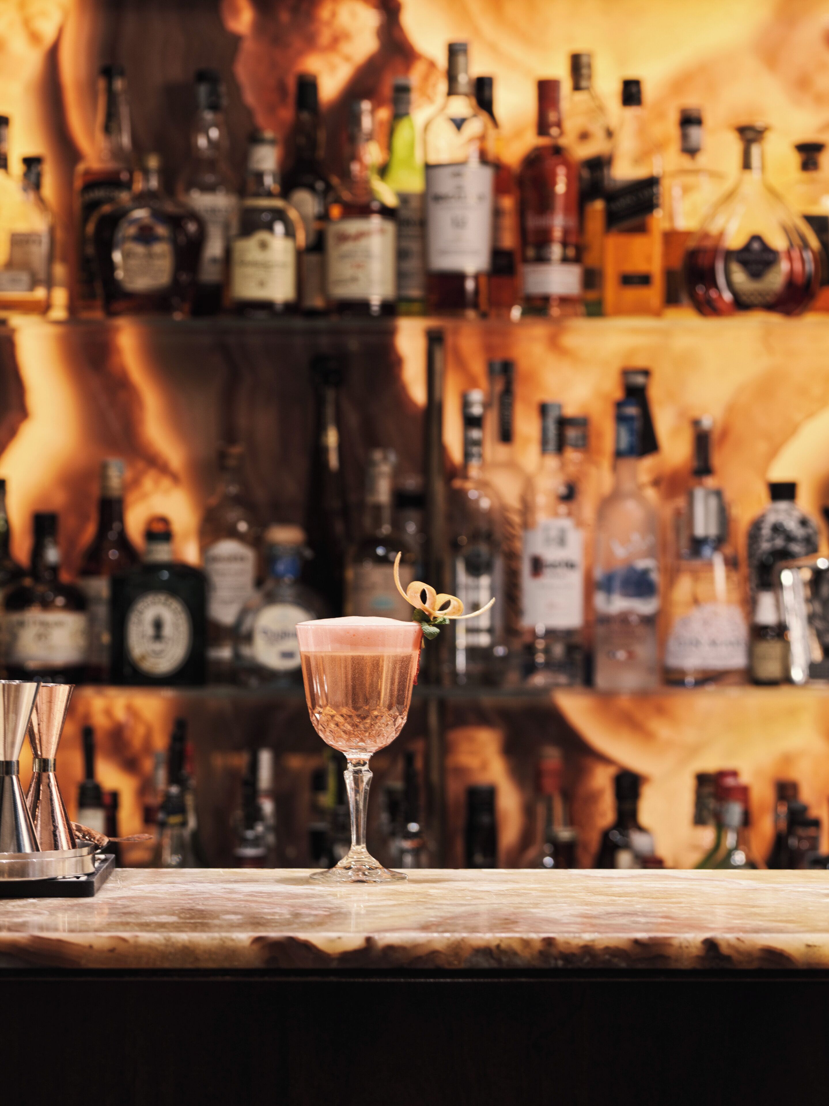 A bar with a variety of liquor bottles in the background and a cocktail glass with a garnish on the counter.