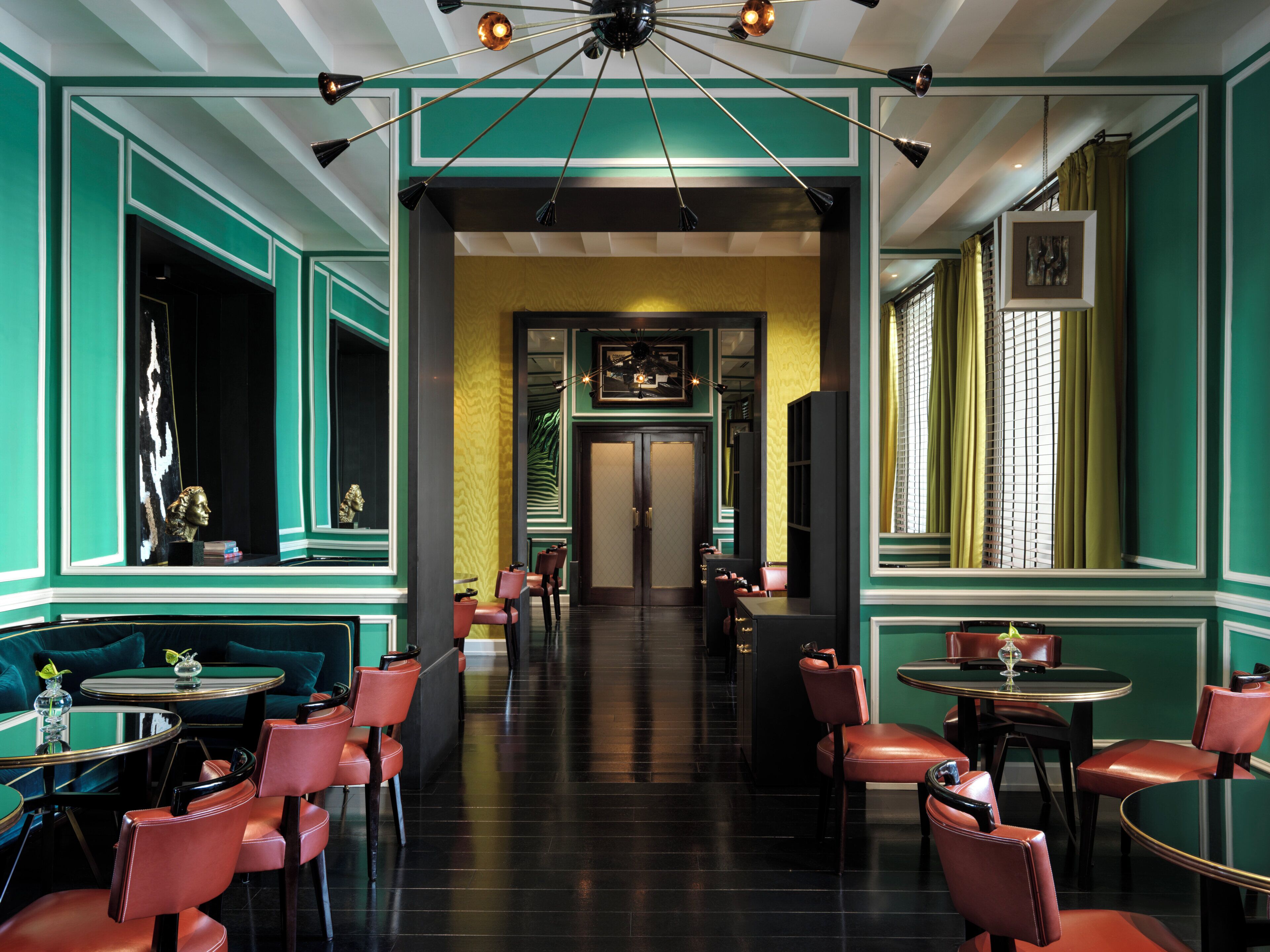 A restaurant interior with green walls, multiple tables and chairs, and a chandelier.