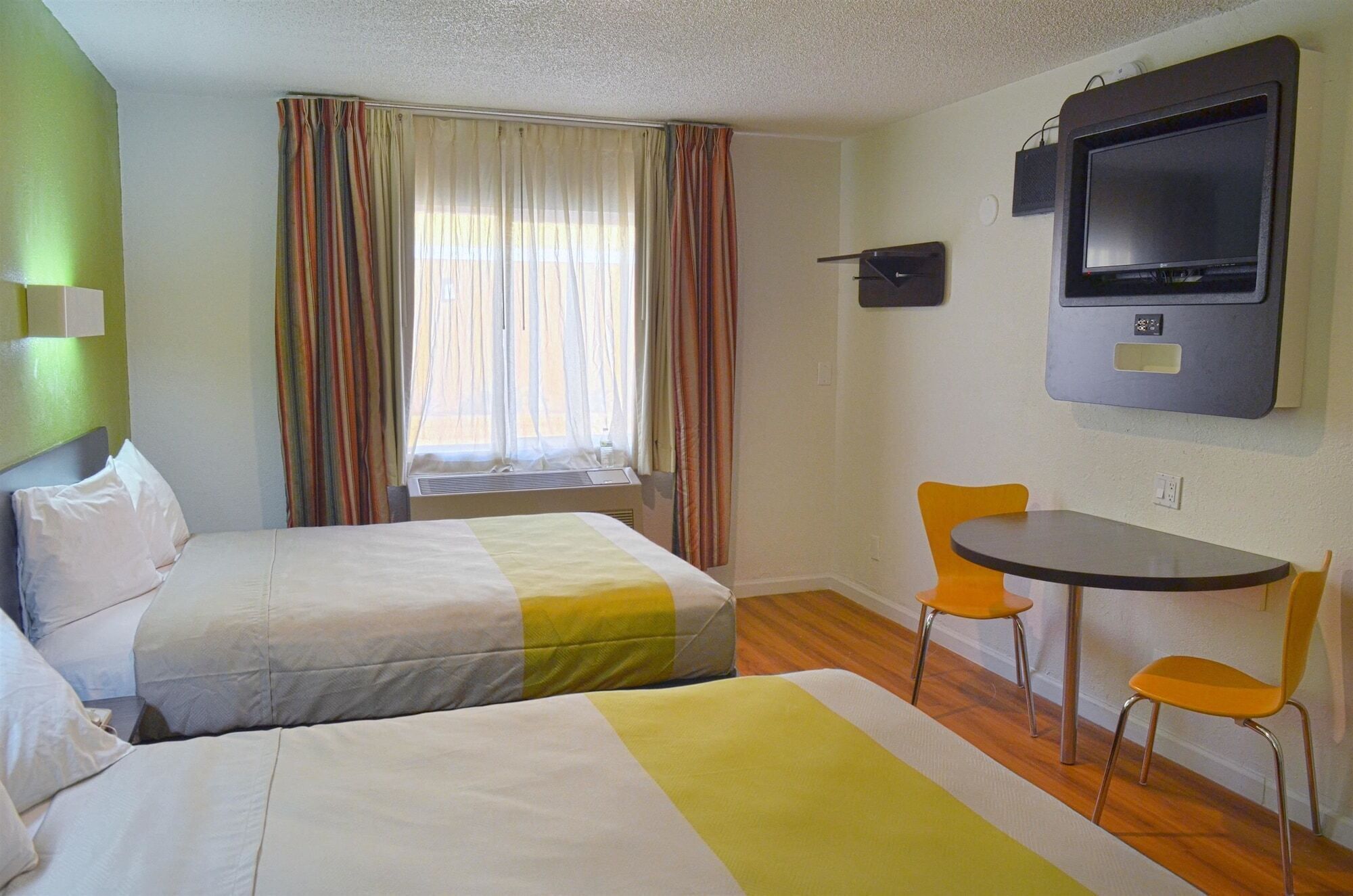 A hotel room with two beds, a TV, and a small table with chairs.