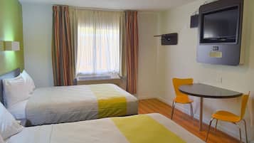 A hotel room with two beds, a TV, and a small table with chairs.