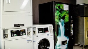 Uma lavanderia com máquinas de lavar e secar empilhadas, uma máquina de lavar industrial e uma geladeira.