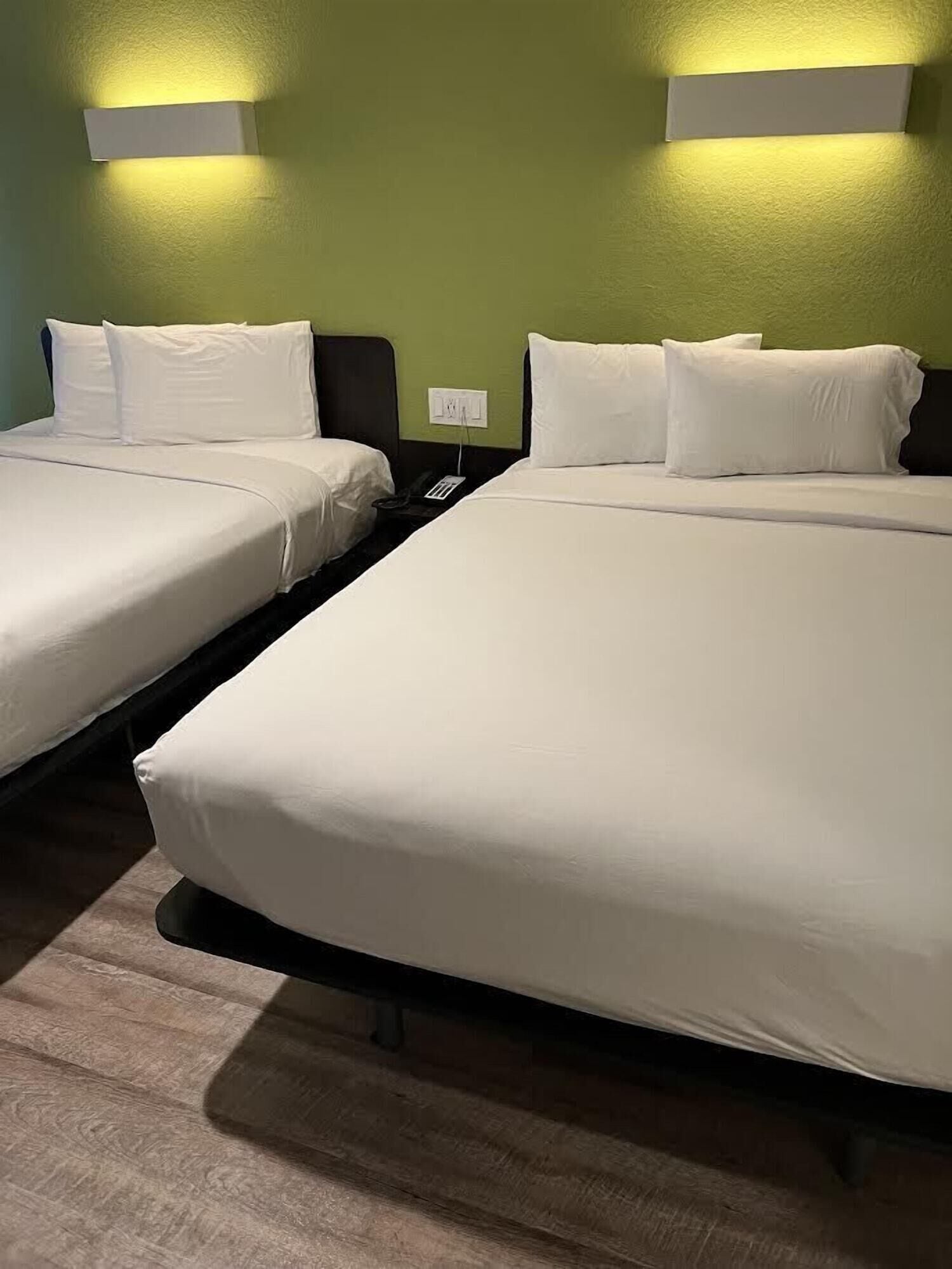A hotel room with two beds, a green wall, and a wall-mounted light fixture.