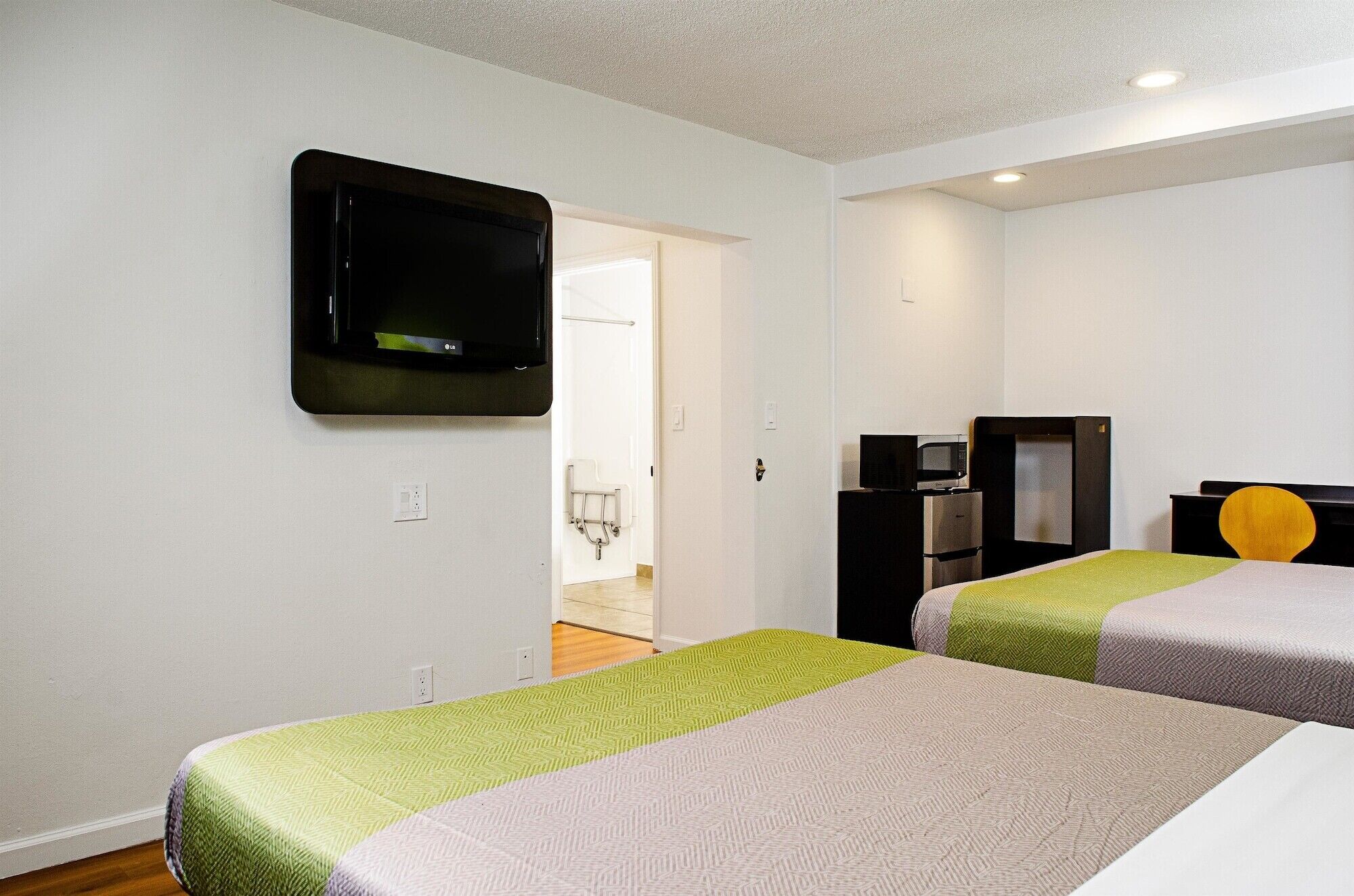 A hotel room with two beds, a flat-screen TV mounted on the wall, a microwave, and a small kitchenette.
