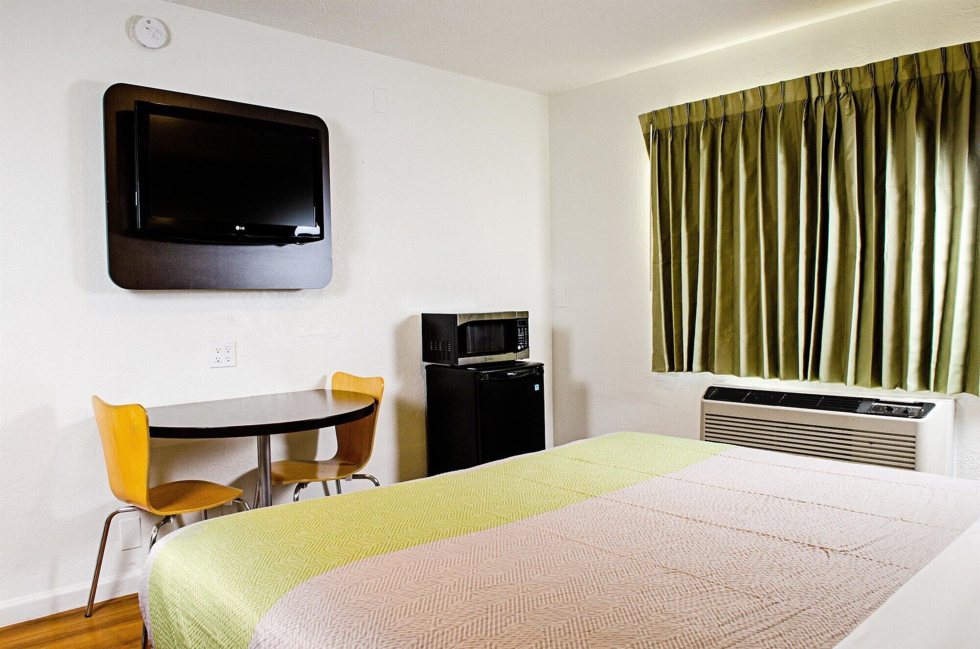 A hotel room with a bed, a desk with two chairs, a television, a microwave, and a heater.