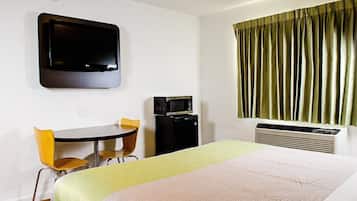 A hotel room with a bed, a desk with two chairs, a television, a microwave, and a heater.