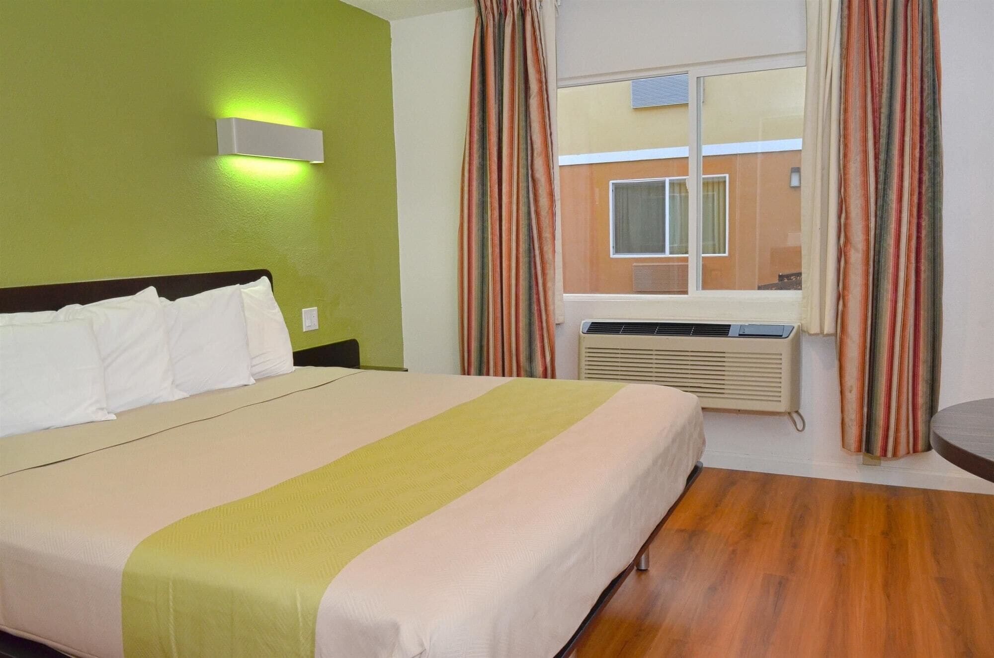 Habitación de hotel con cama, ventana con cortinas, aire acondicionado y vista del edificio exterior.