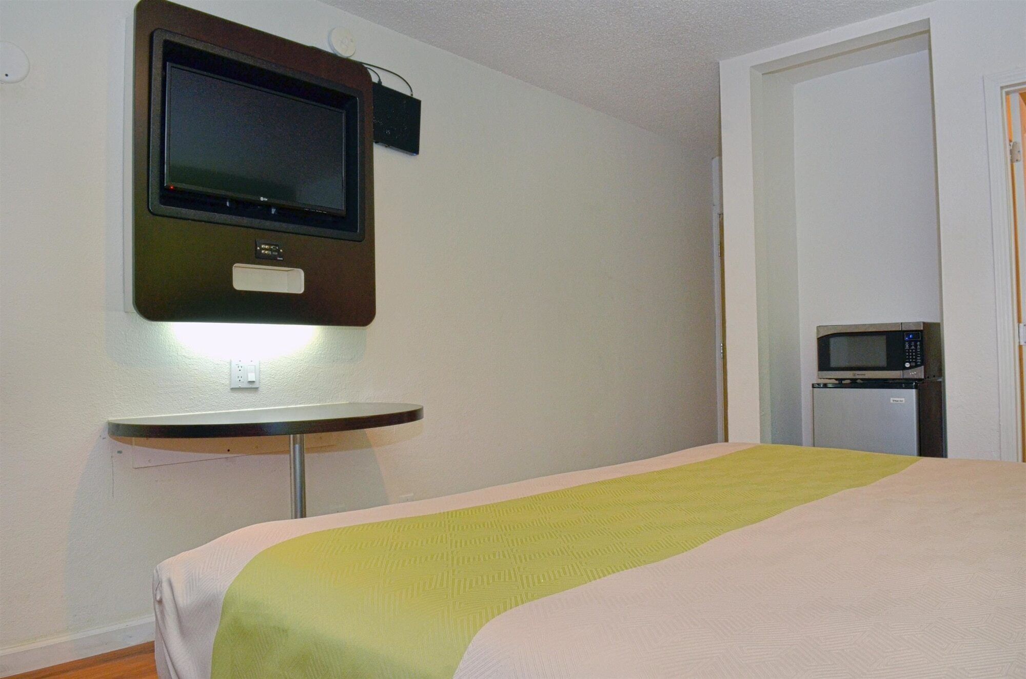 A hotel room with a bed, a TV mounted on the wall, and a microwave on a small table.
