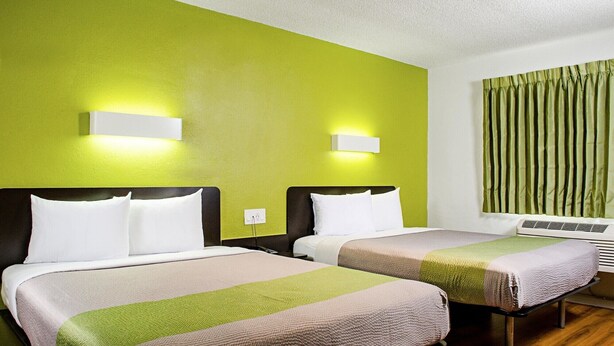 Quarto de hotel com duas camas, paredes verdes e uma janela com cortinas.