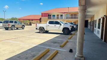 A parking lot with a white pickup truck and a beige SUV. There are yellow bollards and a building with multiple doors and windows in the background.