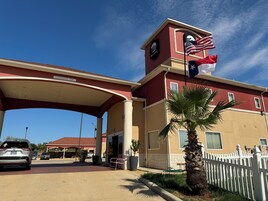 Entrada de hotel con fachada roja y beige, una bandera estadounidense y una palmera en primer plano.