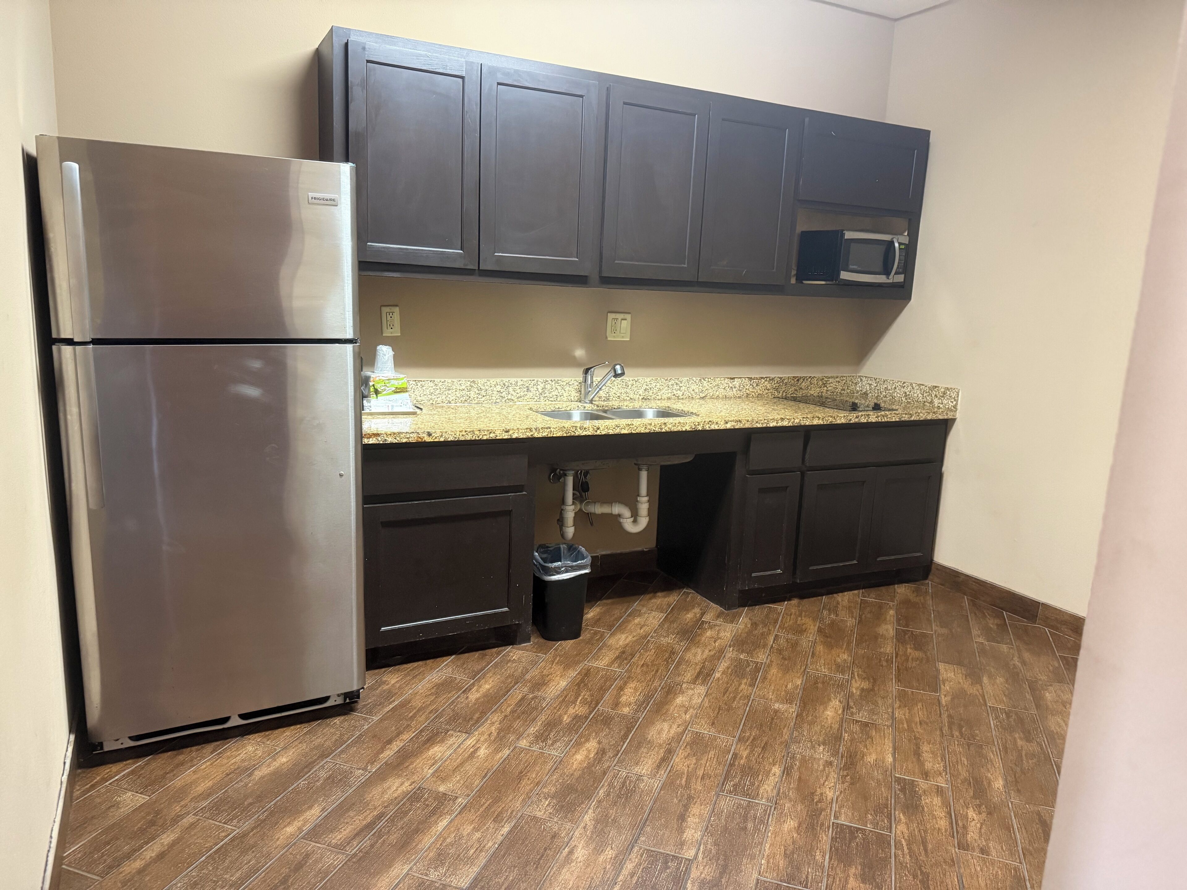 A kitchen with dark cabinets, a stainless steel refrigerator, a granite countertop, a sink, and a microwave.