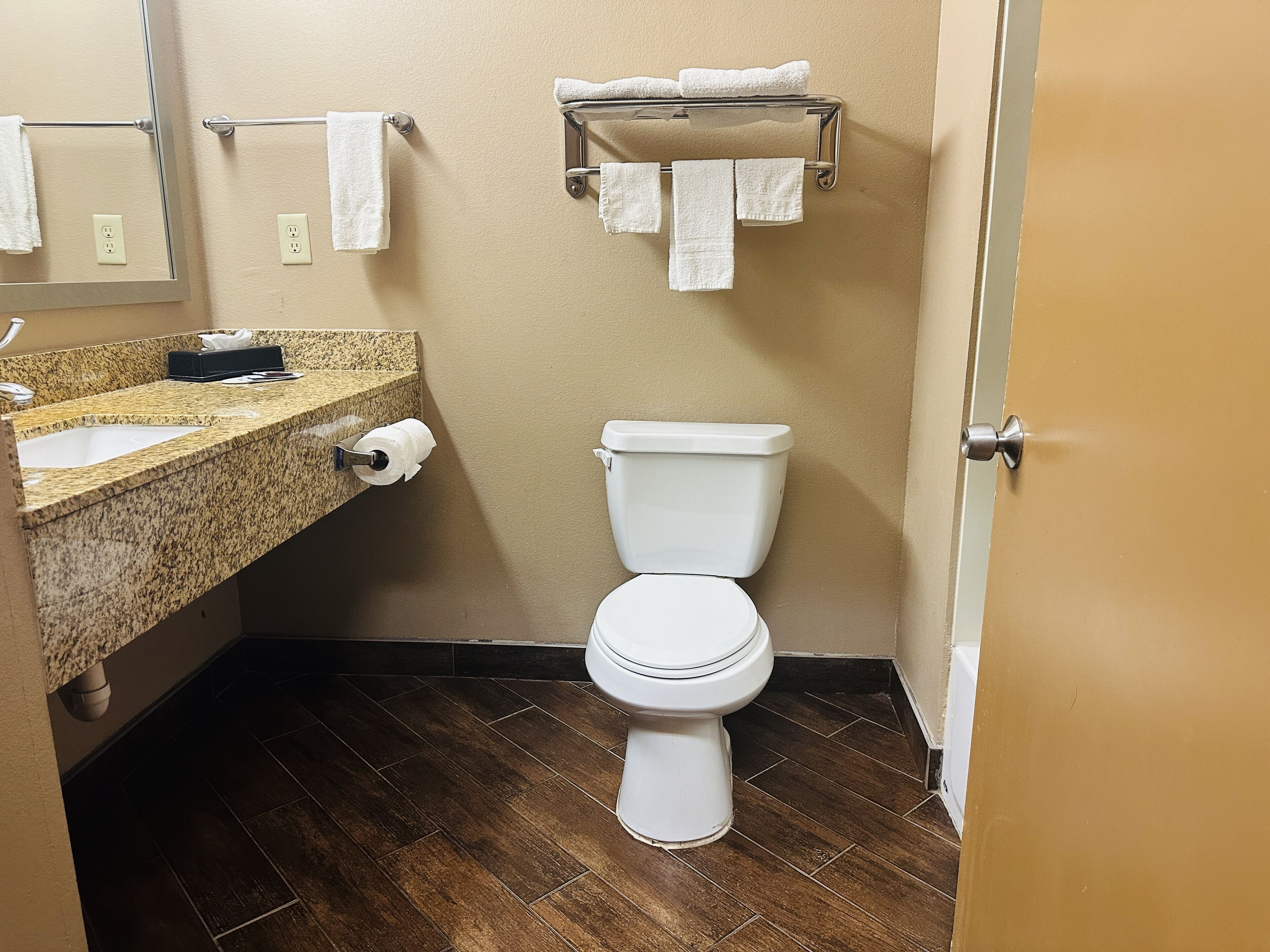 A bathroom with a toilet, a sink with a marble countertop, a towel rack with multiple towels, and a mirror.